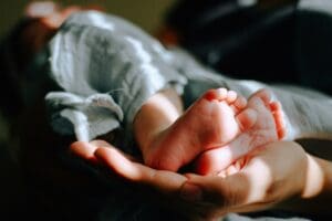 Photo by https://unsplash.com/@omarlopez1Close-up of a baby's tiny feet cradled gently in an adult's hand, symbolizing care, love, and nurturing on the journey of overcoming infertility.