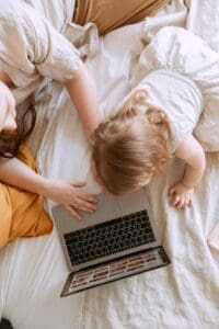 Photo by Tatiana Syrikova Overhead view of a mother and her young daughter typing on a laptop together while lying on a bed, symbolizing connection, nurturing, and exploring infertility solutions.